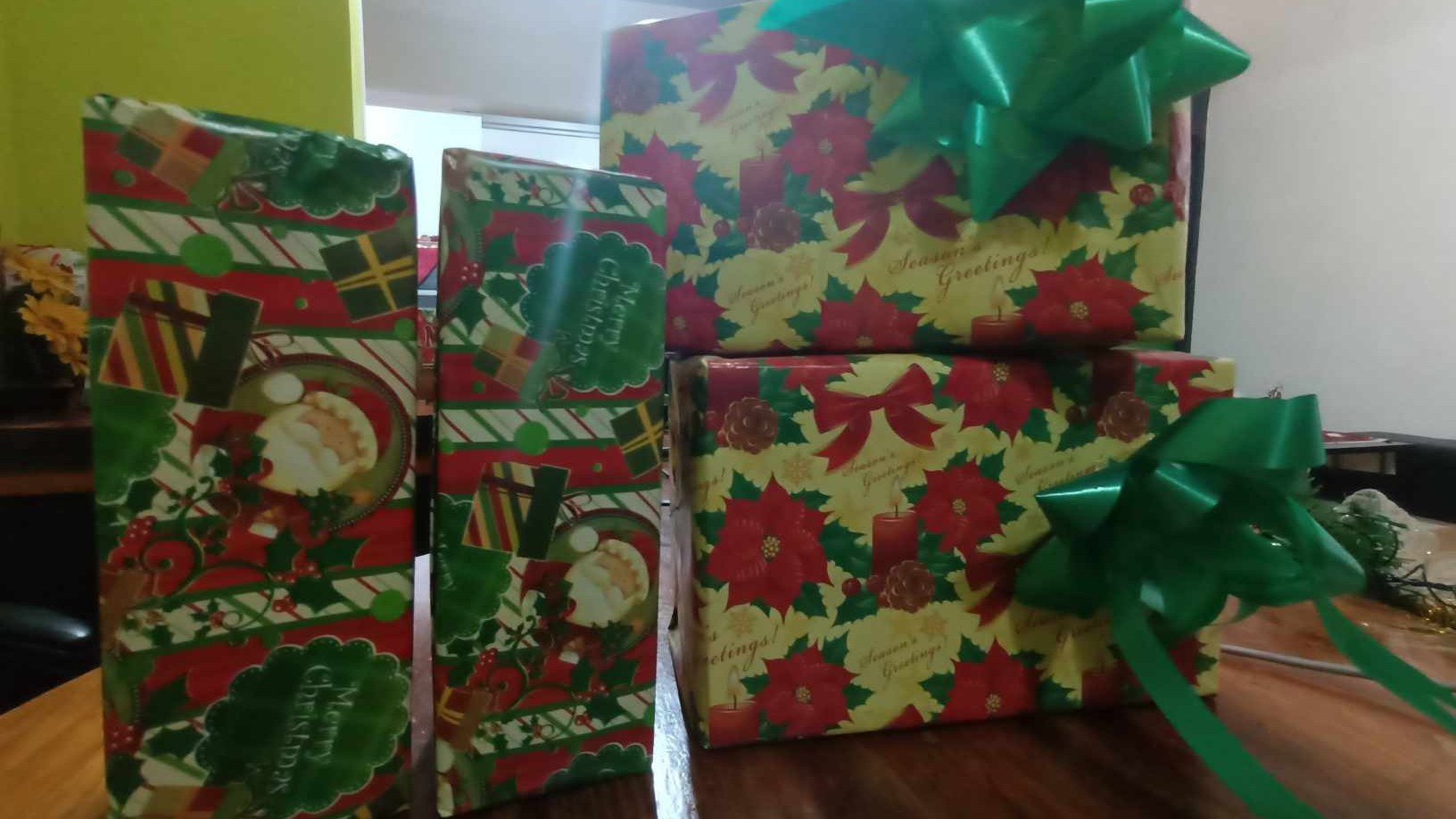 Cuatro regalos de Navidad envueltos en papel con flores de Pascua y Papá Noel, con lazos verdes, sobre una mesa de madera